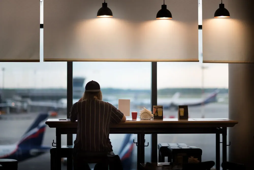 Person sitting at an airport cafe looking out the window at the airplanes on the runway